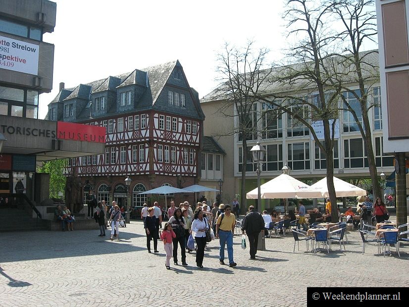 Links het Historisches Museum. Het vakwerkhuis is het restaurant Haus Wertheym (1479). Je loopt tussen deze gebouwen door naar de voetbrug over de rivier Main.