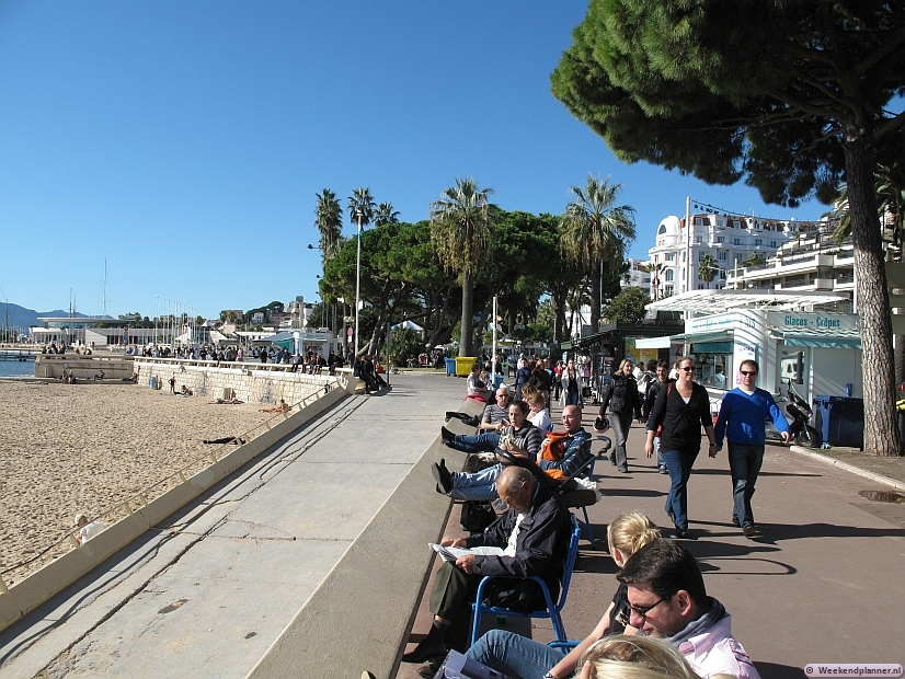 De promenade langs het strand en de de Boulevard de la Croisette. Links bij het strand in zee zie je het beroemde gebouw voor de festivals en de congressen, het Palais des Festivals et des Congrès de Cannes. Er is ook een casino.