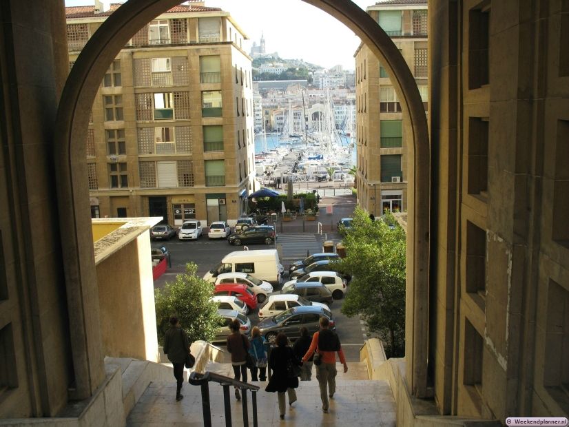 Vanuit de oude haven kun je naar de oude wijk van Marseille. Op de achtergrond zie je de 19de-eeuwse Basilique de Notre Dame de la Garde. Deze kathedraal is van verre op zee zien. Tips: Een weekend in Marseille.