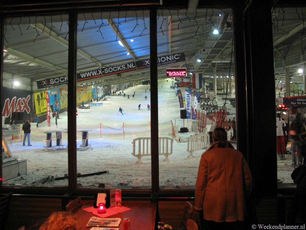 Het uitzicht op de skihal vanuit de restaurants. Als je zelf niet wilt skiën of als je wilt uitrusten na het skiën is het leuk om hier naar het skiën en snowboarden te gaan kijken. Tips: Skiën en snowboarden in Landgraaf.